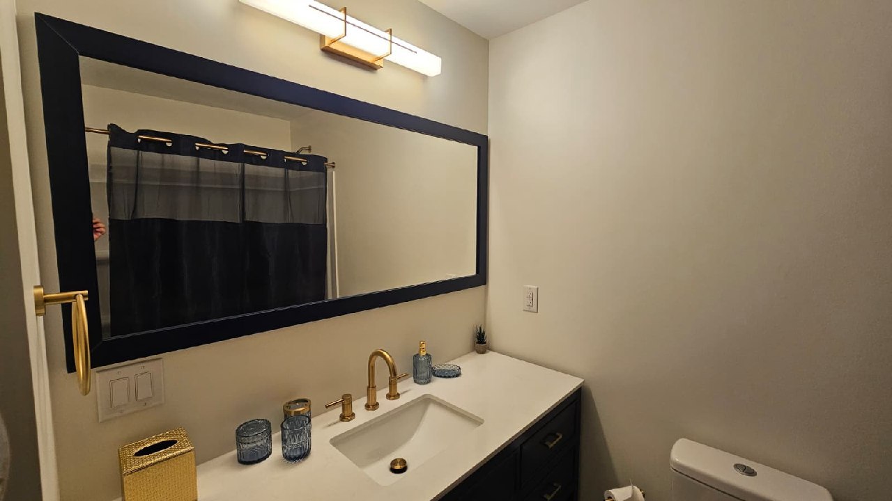 Hall bathroom vanity with gold faucet, navy mirror, and designer accessories